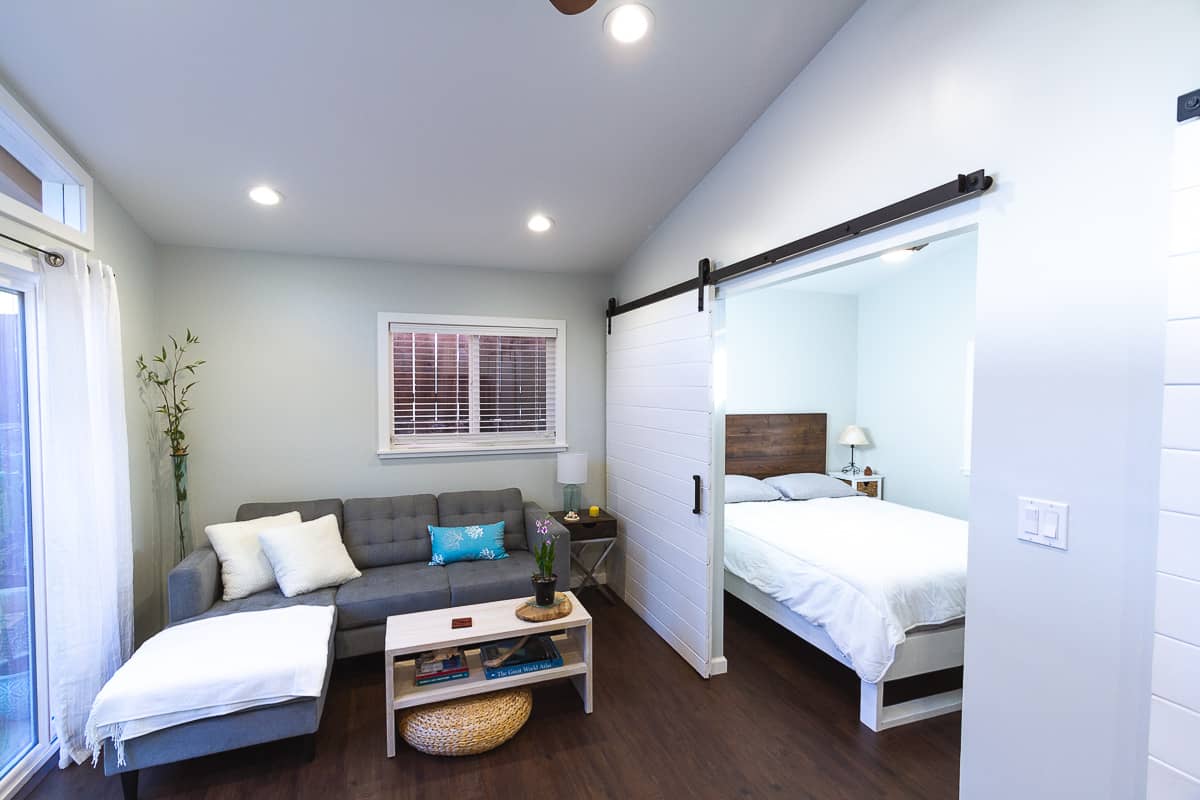 Living room ,gray couch, white barn door separating the bedroom