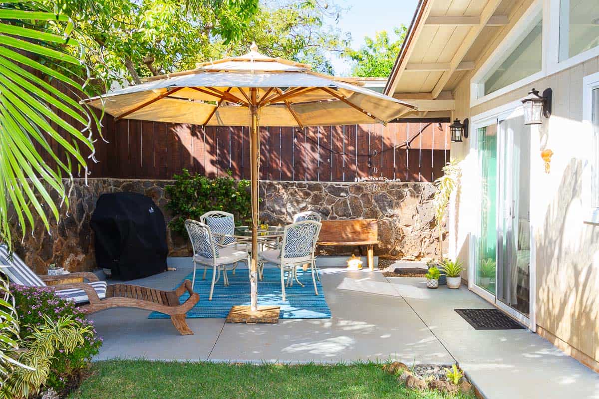 Outdoor patio with large standing umbrella, lounge change, dining table and entrance to guest house