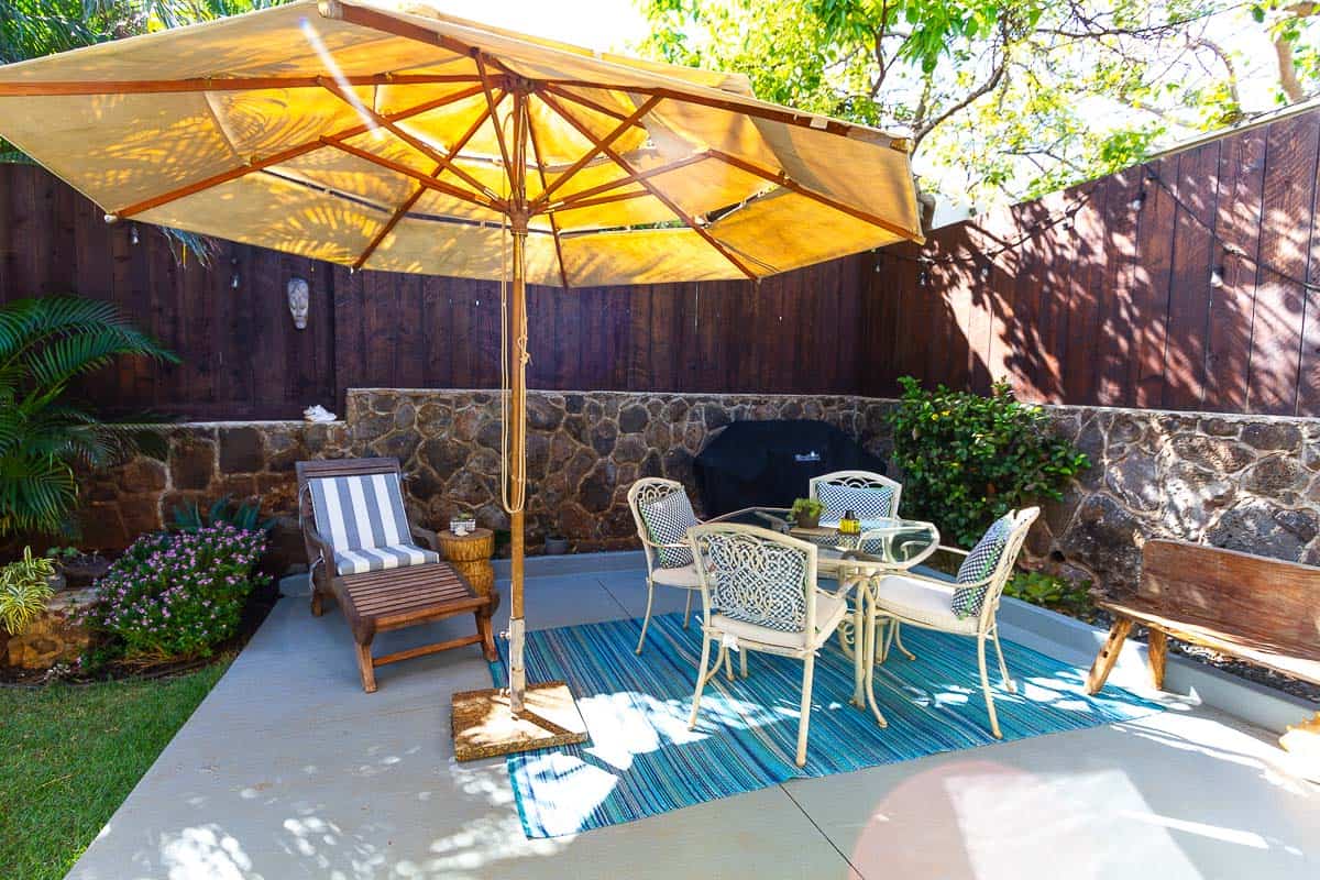 Outdoor patio with large standing umbrella, lounge change and dining table.