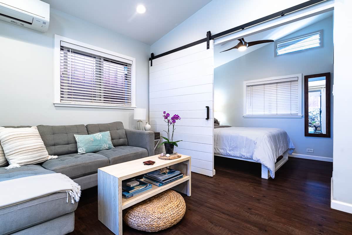 Living area with gray sectional sofa and coffee table, separated from the bedroom by a white sliding barn door.