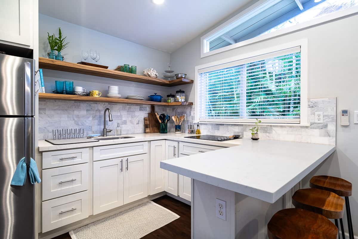 Kitchen with white cabinets, stainless steel refrigerator, open wood shelves, and a breakfast bar with stools.